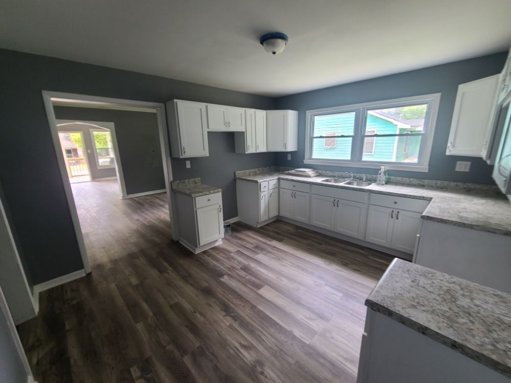 Empty modern kitchen with gray cabinets, wood-look floors, and a bright window.
