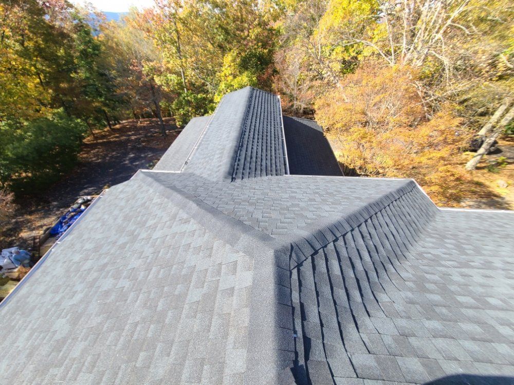 Gray shingled roof with central ridge, viewed from above, surrounded by autumn trees