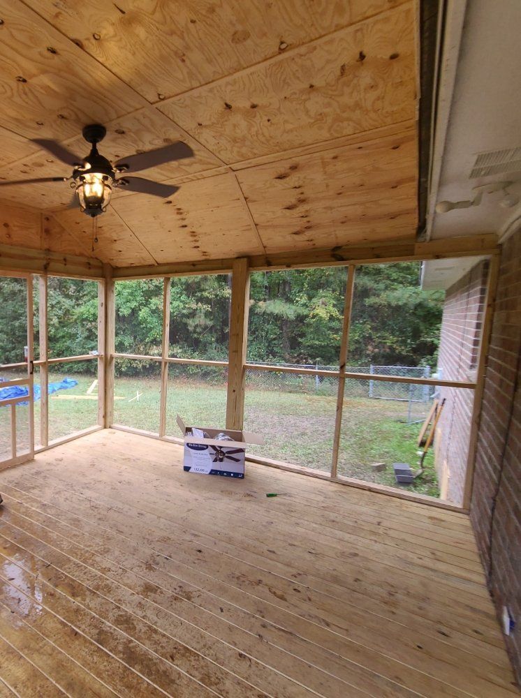 Unfinished screened porch with plywood floor and ceiling, ceiling fan, and view of a backyard and pond.