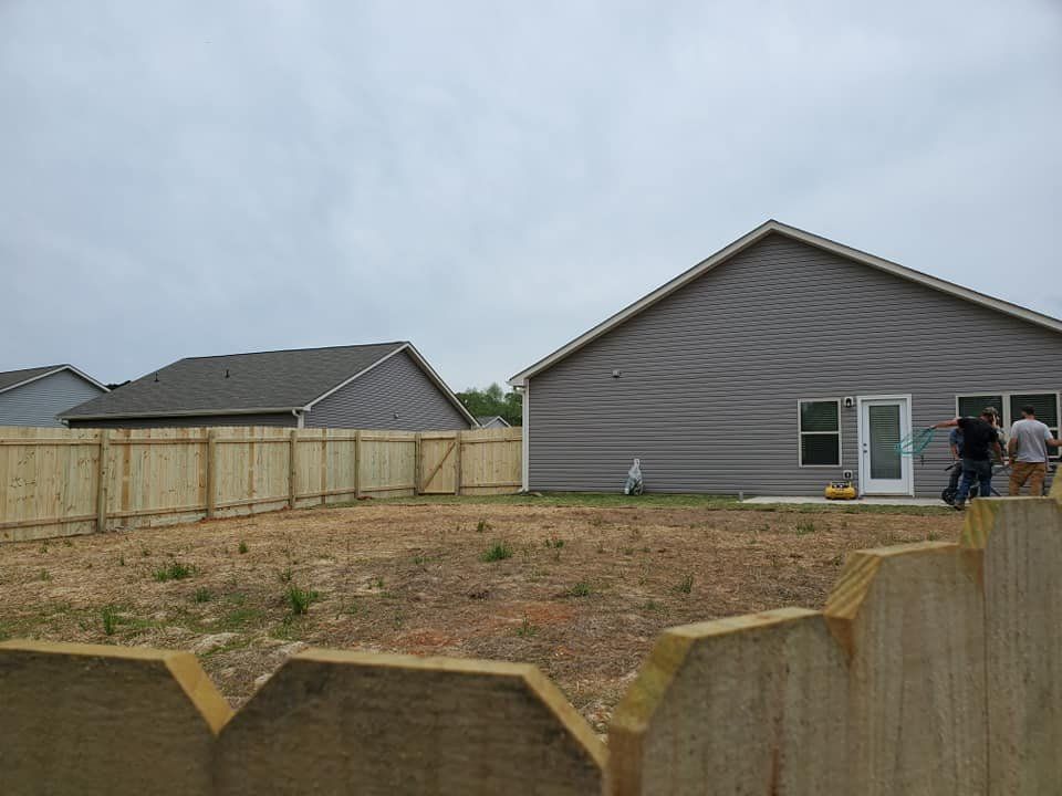 New houses with fenced dirt yard and workers near a gray home