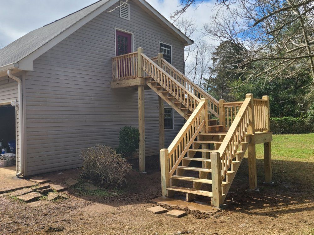 Wooden exterior staircase and landing added to a gray house, with a ramp and railings in the yard