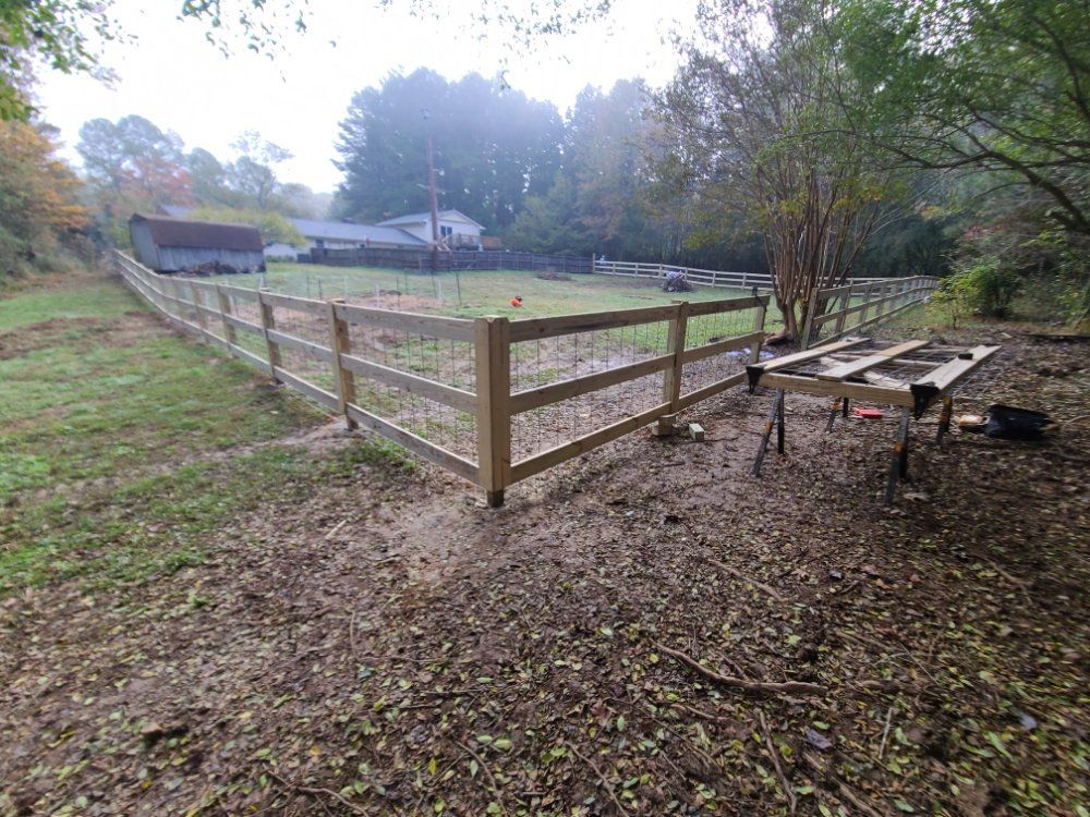 Wooden fenced animal pen beside a gravel area, with picnic tables and trees in a misty yard.