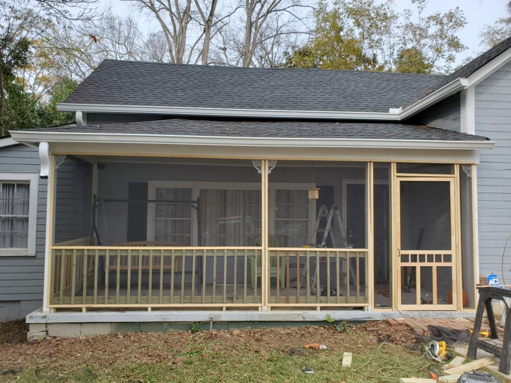 Gray house front porch under construction with unfinished wooden railing and screened sections