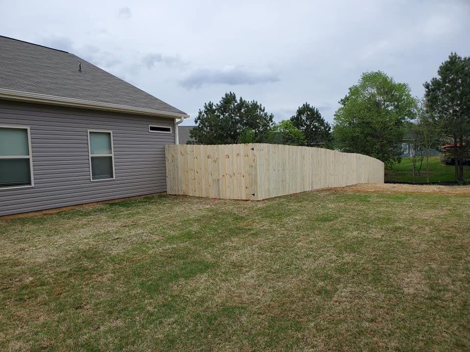 Backyard beside a gray house with a long wooden privacy fence under cloudy skies