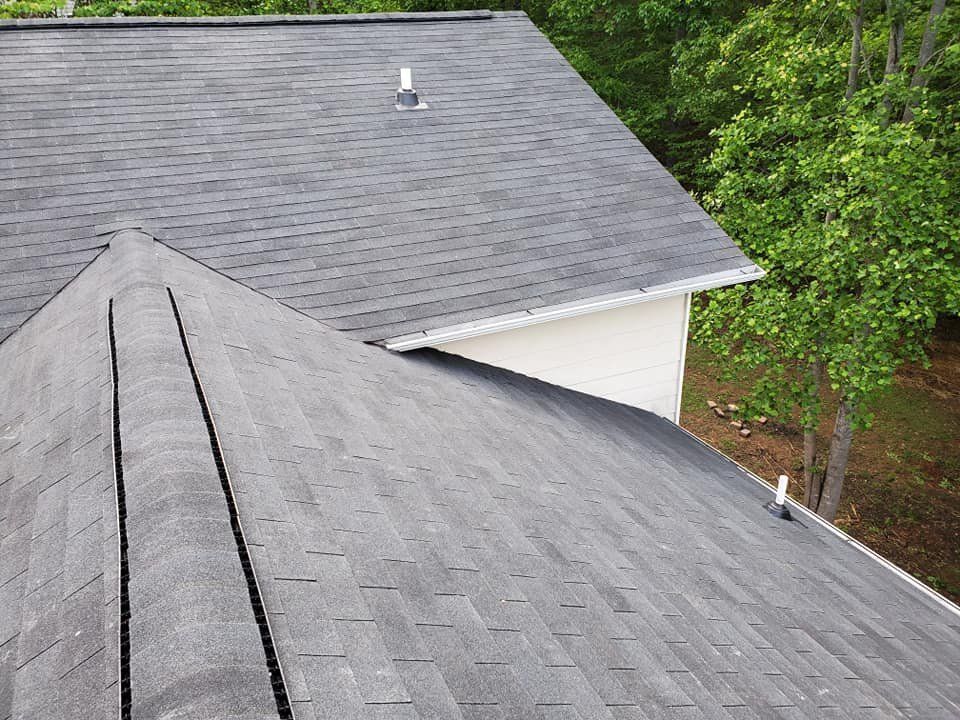 Gray shingle roofs on a house beside green trees, viewed from above