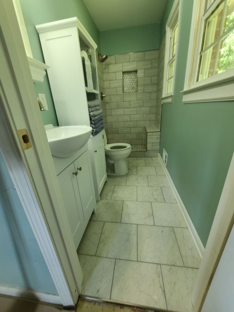 Narrow green bathroom with white tiled floor, shower at the back, toilet, sink, and window light.