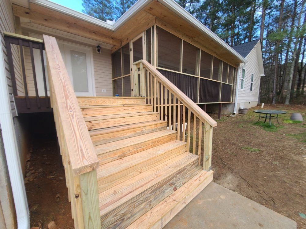 Wooden front porch stairs and ramp with railings on a beige house in a wooded yard