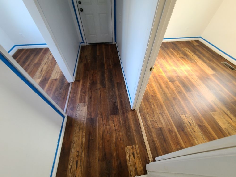 Hallway with dark wood floors and white doors leading into two rooms with blue painter’s tape along the walls