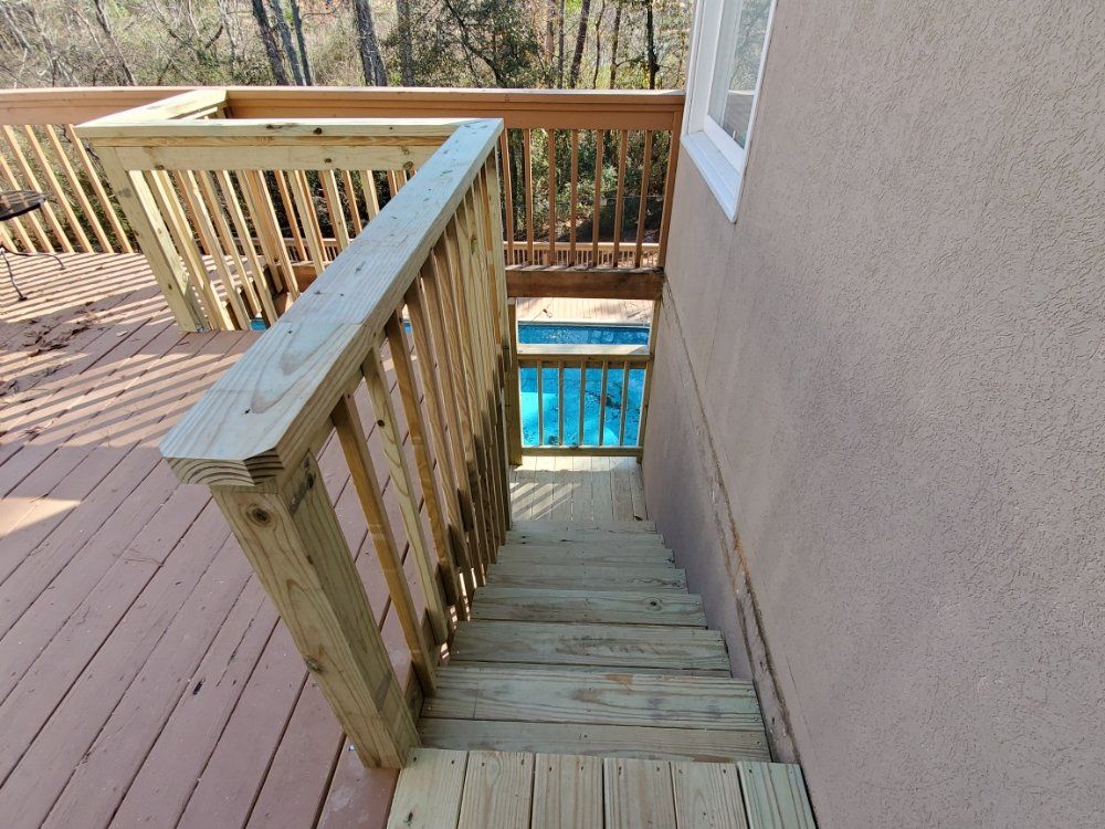 Wooden deck stairs with railing leading down to a blue pool beside a house