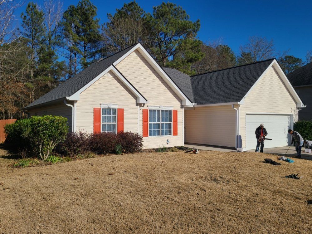 Suburban beige house with red shutters and a person standing by the garage in a front yard