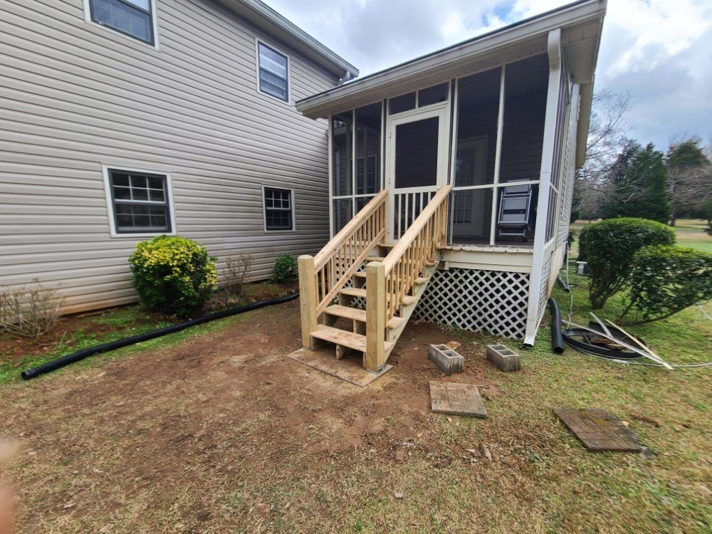 Small backyard porch with wooden stairs and screened entry beside a beige house.