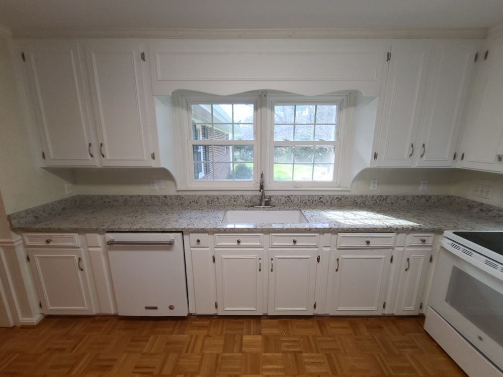 White kitchen with granite countertops, central window, and hardwood floor