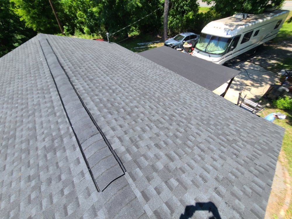 Roof shingles and a roof vent on a house beside an RV and trees
