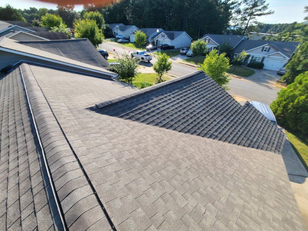 Aerial view of gray shingle rooftops in a suburban neighborhood with trees and houses in the background