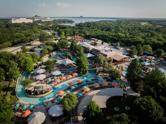 Aerial view of a tropical resort with turquoise pools, palm trees, and lounge chairs near the coast.