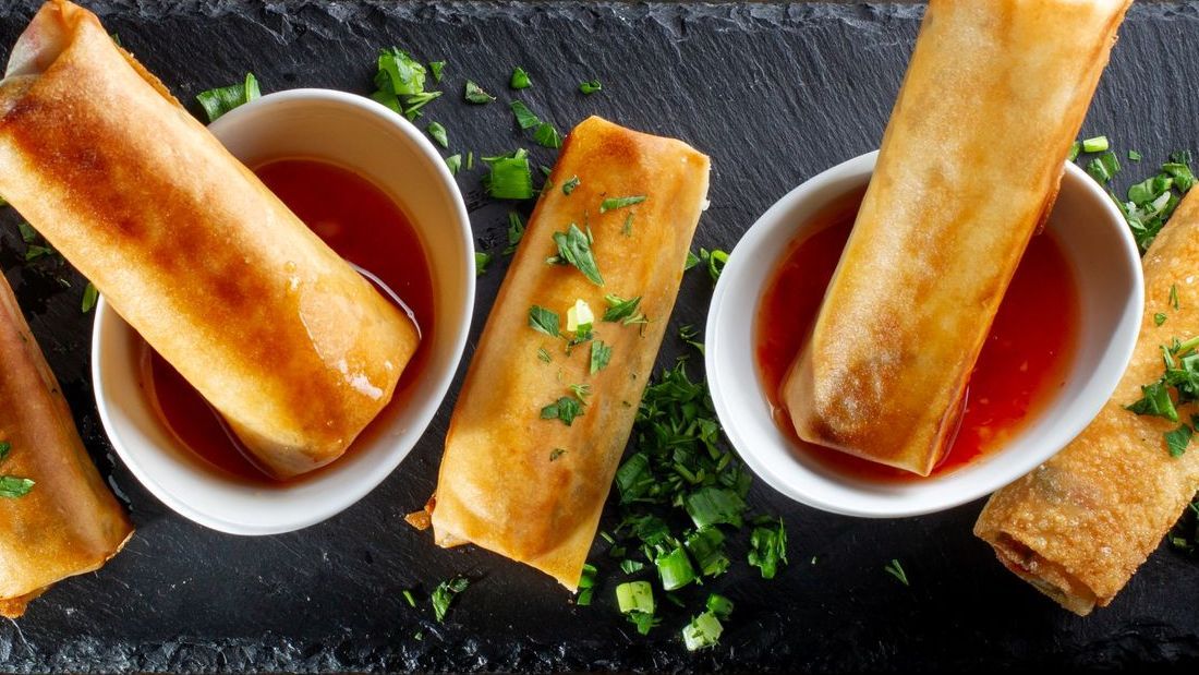 Spring rolls dipping into sweet chilli sauce 