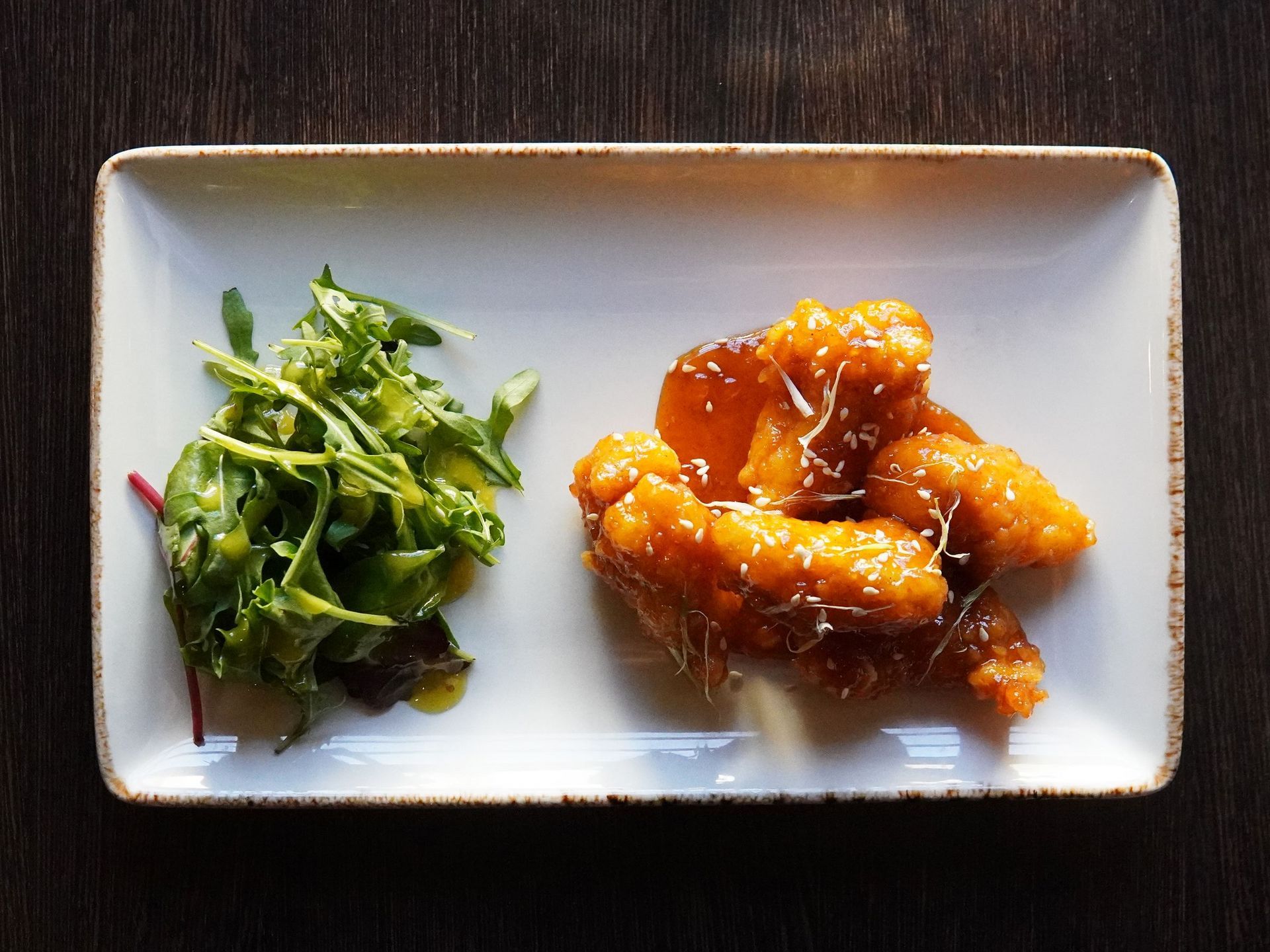 honey chilli chicken on a white plate next to fresh salad