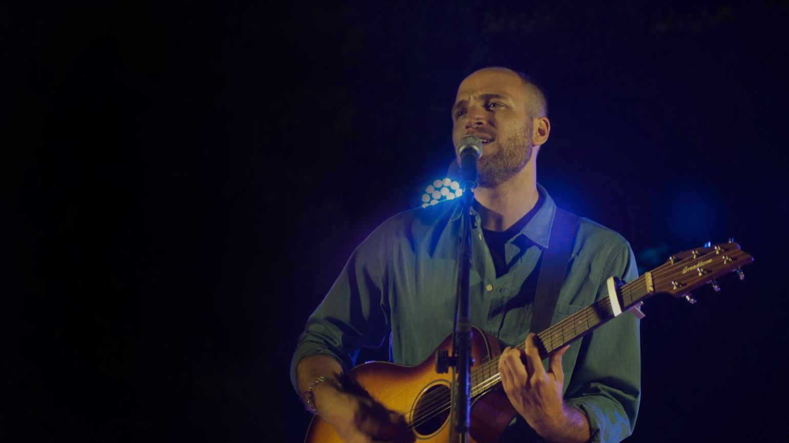 Jeremy Levif singing into a microphone while playing guitar