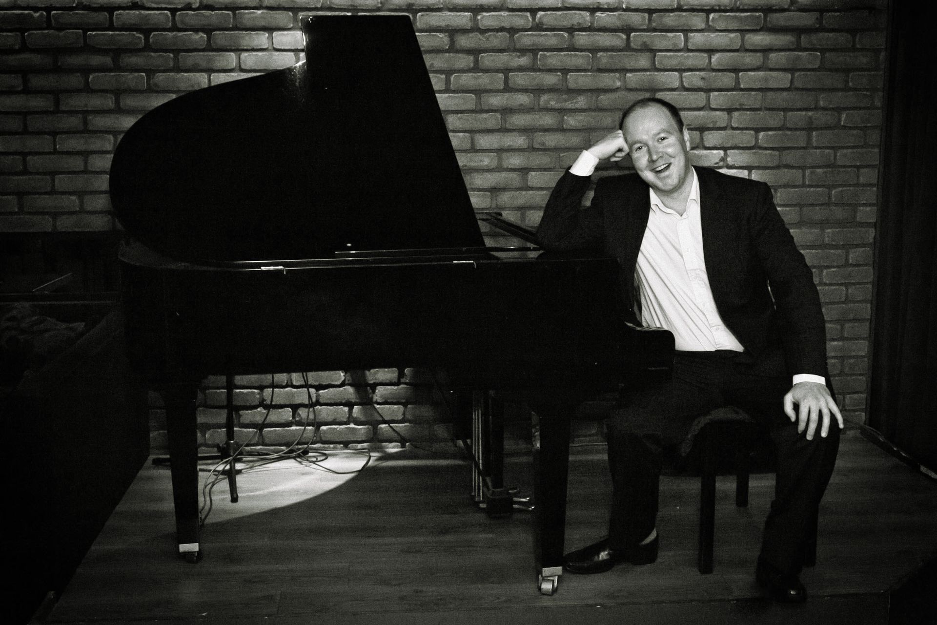 John Rankin wearing a suit sitting at a grand piano smiling at camera