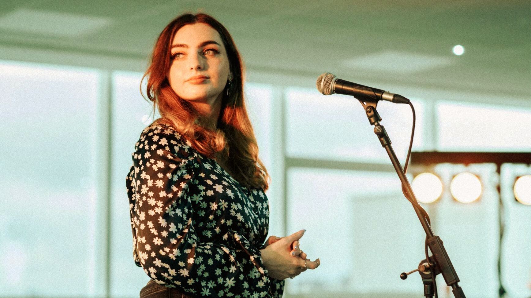 Rebekah Kirk, a young female singer, standing in front of a microphone