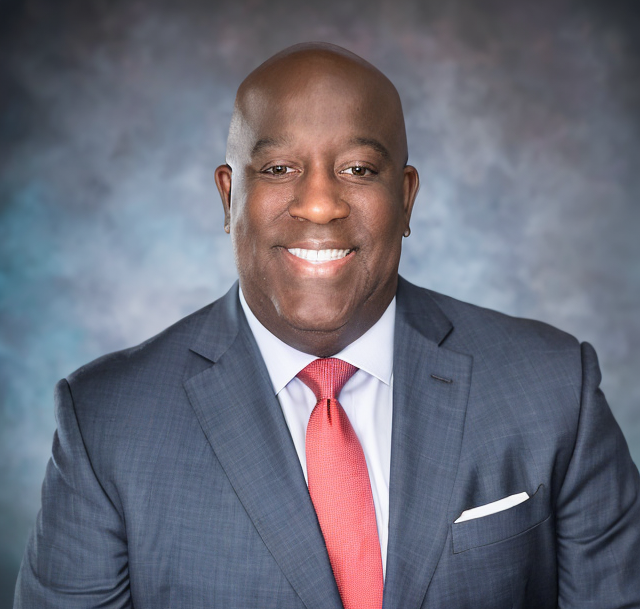 Studio portrait of a smiling man in a blue suit and red tie against a gray backdrop