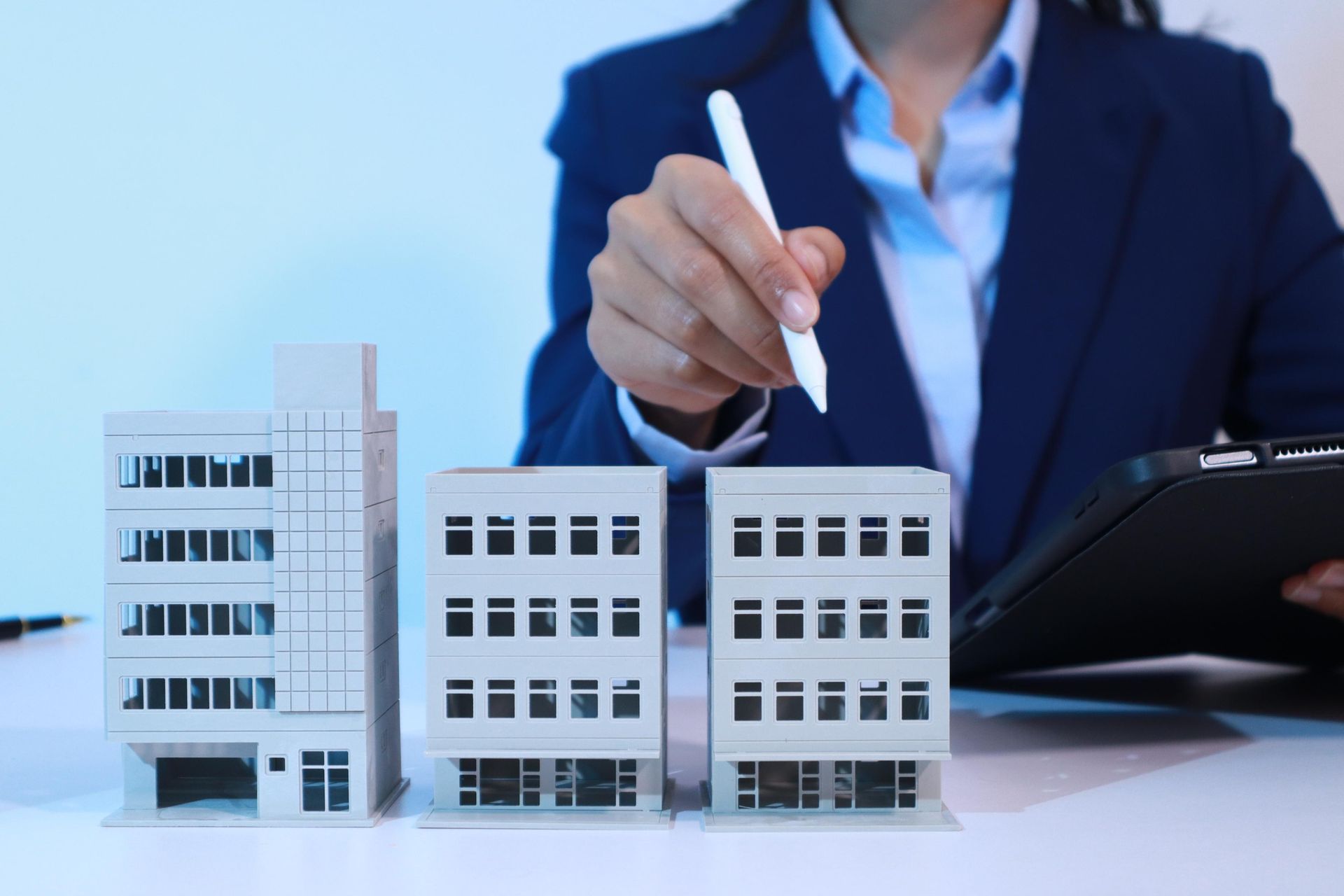 Person in a suit holding a pen above miniature building models.
