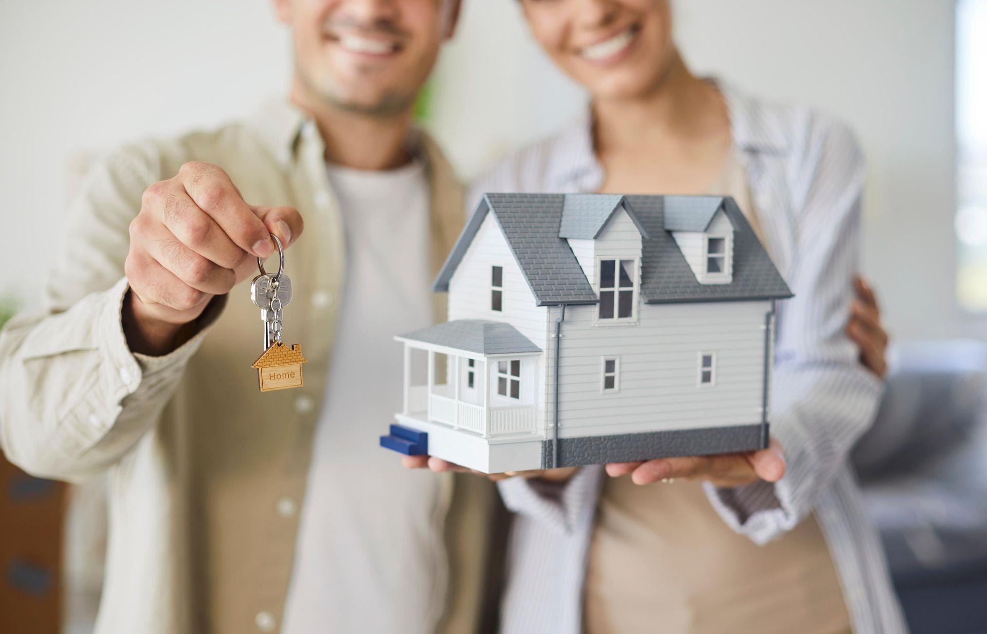 Couple holding house model and keys, smiling.