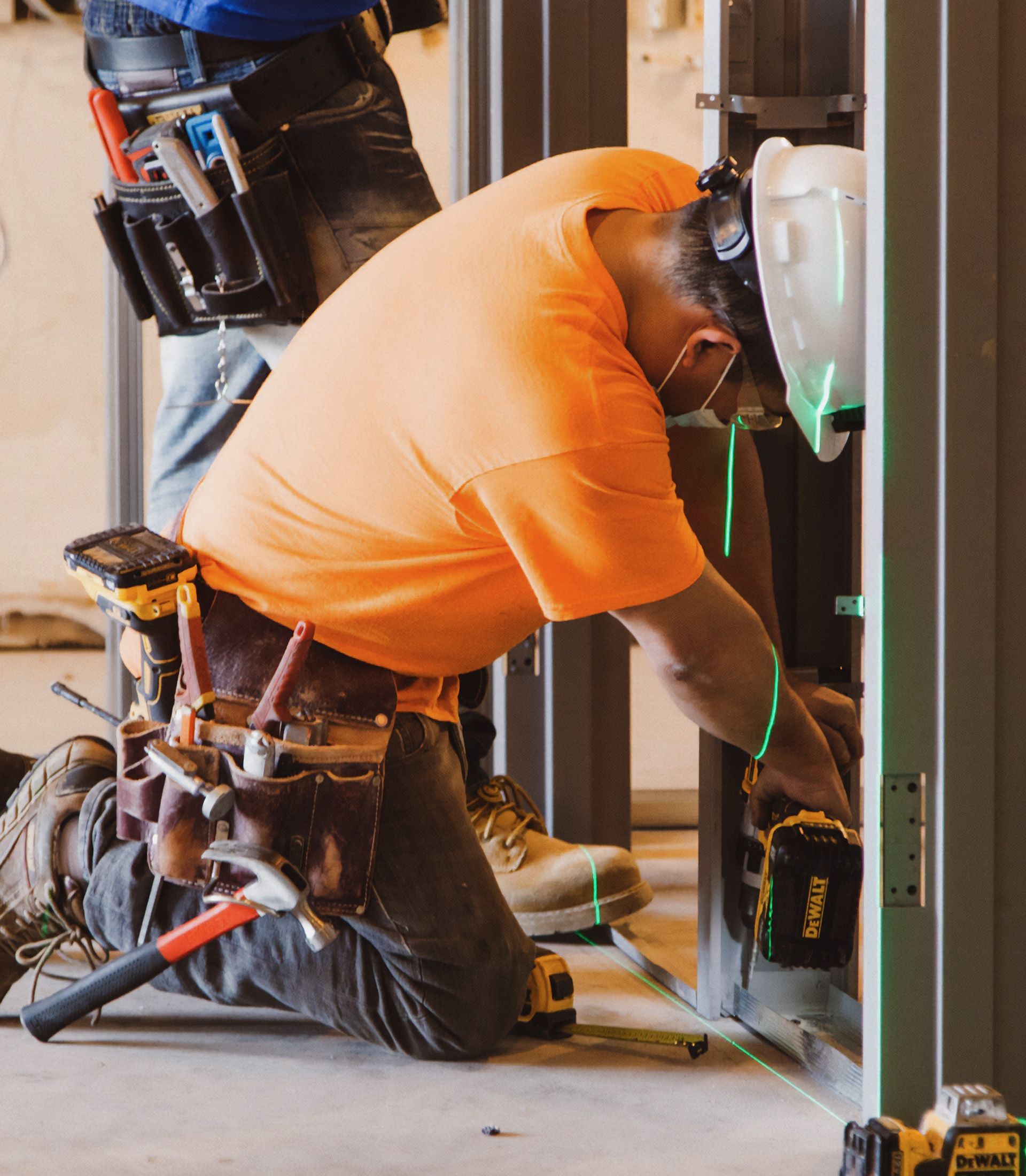 A man in an orange shirt is kneeling down and working on a wall