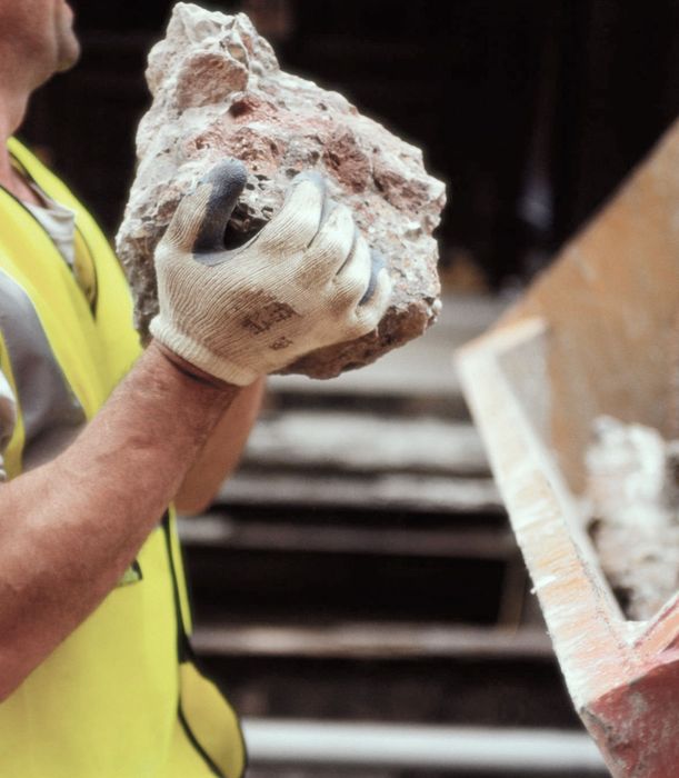 A man wearing a yellow vest and gloves is holding a large rock