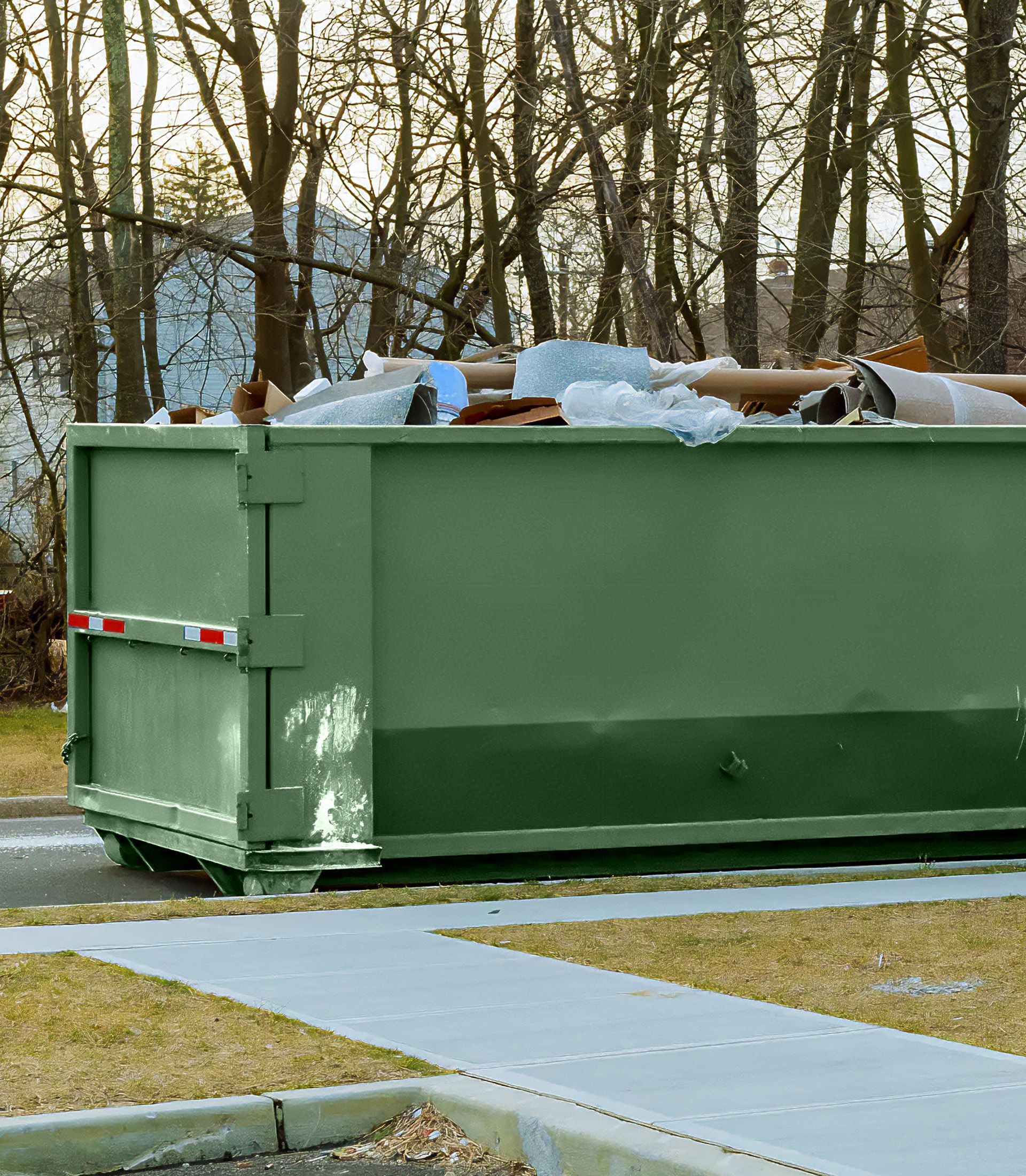 A green dumpster filled with trash is parked on the side of the road.