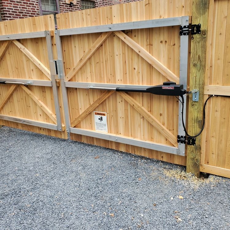 Wooden driveway gate with a black automatic opener arm and gravel ground nearby