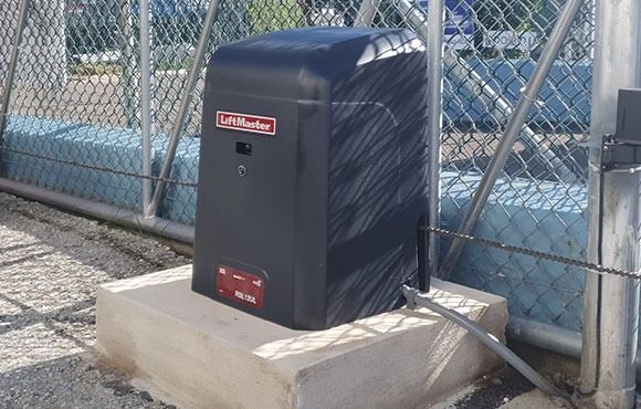 Black utility box on a concrete base beside a chain-link fence outdoors