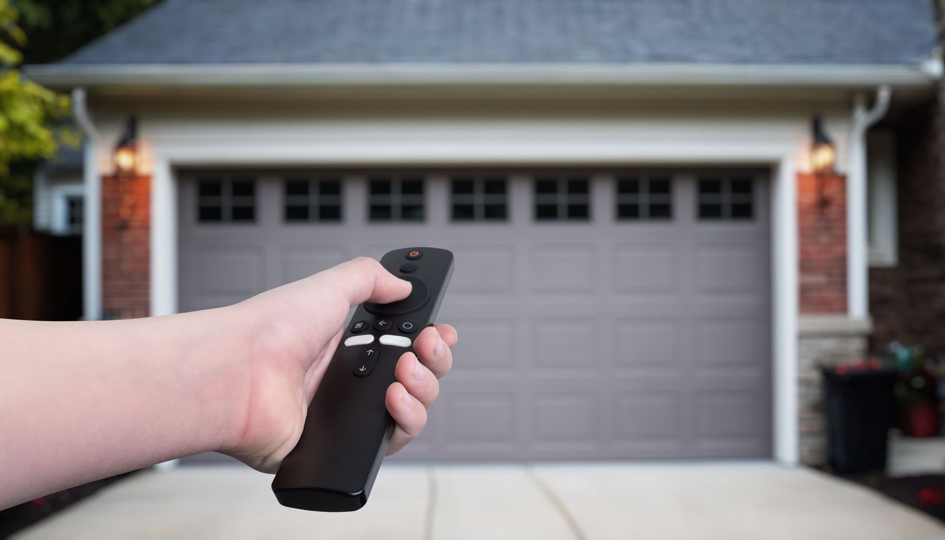 Hand holding a black remote pointed at a closed garage door