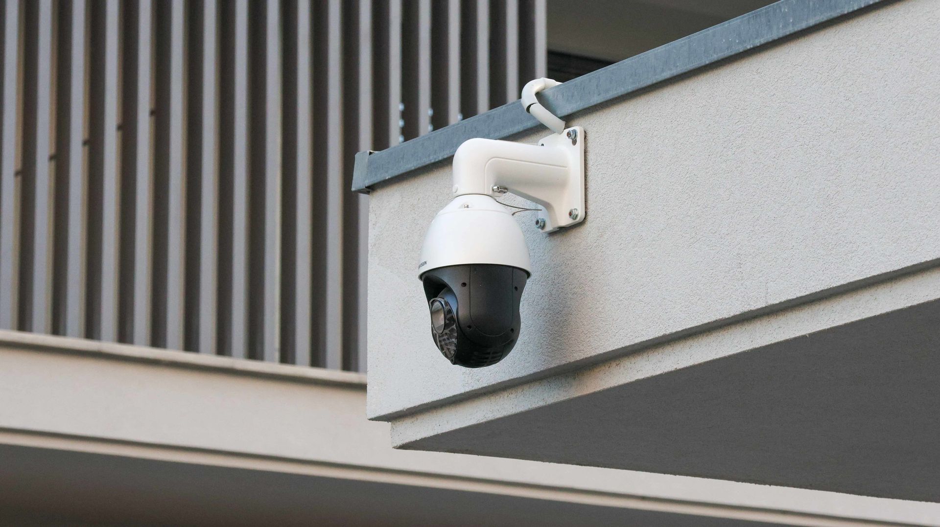 White security camera mounted under a building overhang, angled downward.