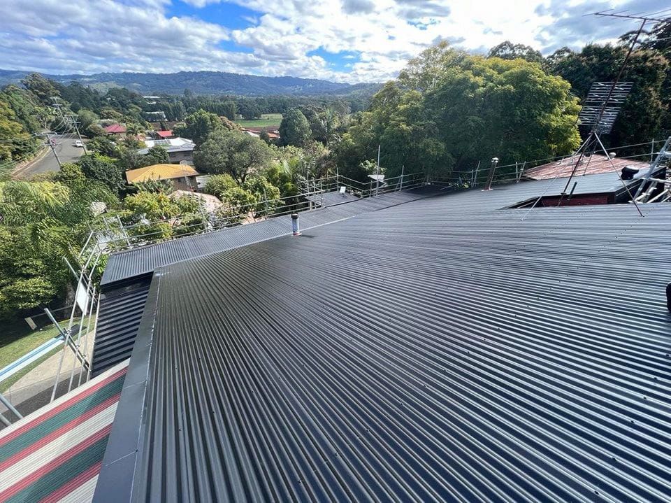 View From a Dark Corrugated Metal Roof Overlooking a Town With Green Trees — Rumara Roofing in Buderim, QLD