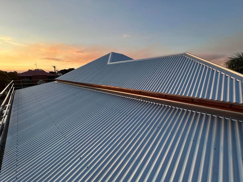 Corrugated Metal Roof at Sunset With a Gradient Sky and Brown Gutter — Rumara Roofing in Mountain Creek, QLD