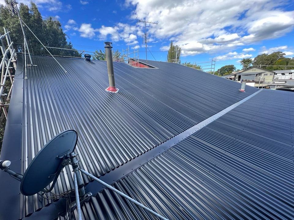 Black Metal Roof With a Chimney and Satellite Dish Under a Blue Sky — Rumara Roofing in Buderim, QLD