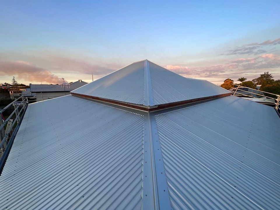 Silver Corrugated Metal Roof With a Peaked Center, Blue Sky Background — Rumara Roofing in Landsborough, QLD
