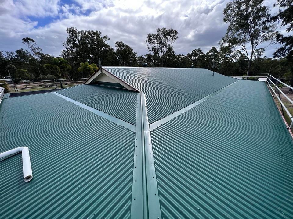 Green Corrugated Metal Roof With Light Sky and Trees in Background — Rumara Roofing in Landsborough, QLD