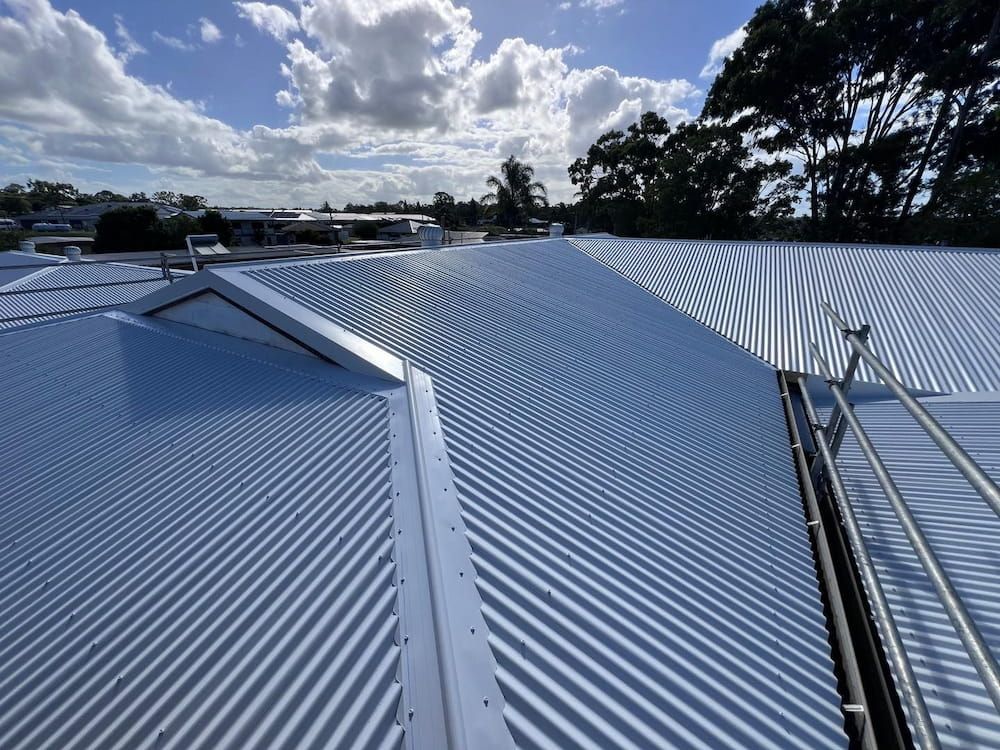 Corrugated Metal Roof With a Skylight and Ladder, Blue Sky in Background — Rumara Roofing in Mountain Creek, QLD