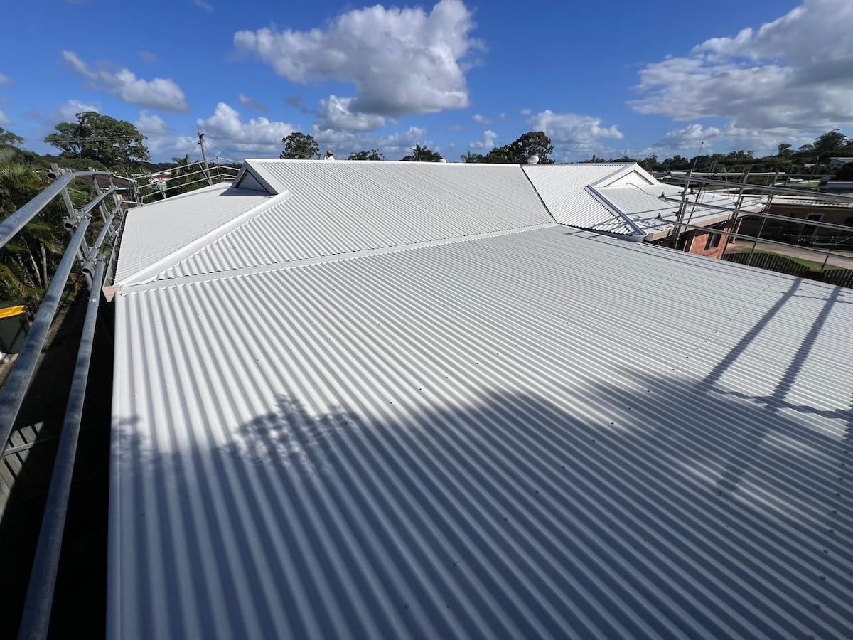 White Corrugated Metal Roof on a Building Under a Blue Sky With Clouds — Rumara Roofing in Sunshine Coast, QLD
