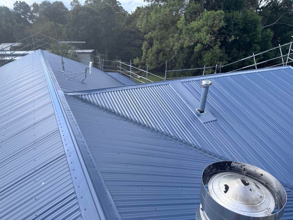 Blue Corrugated Metal Roof With Chimneys and Trees in the Background — Rumara Roofing in Sunshine Coast, QLD