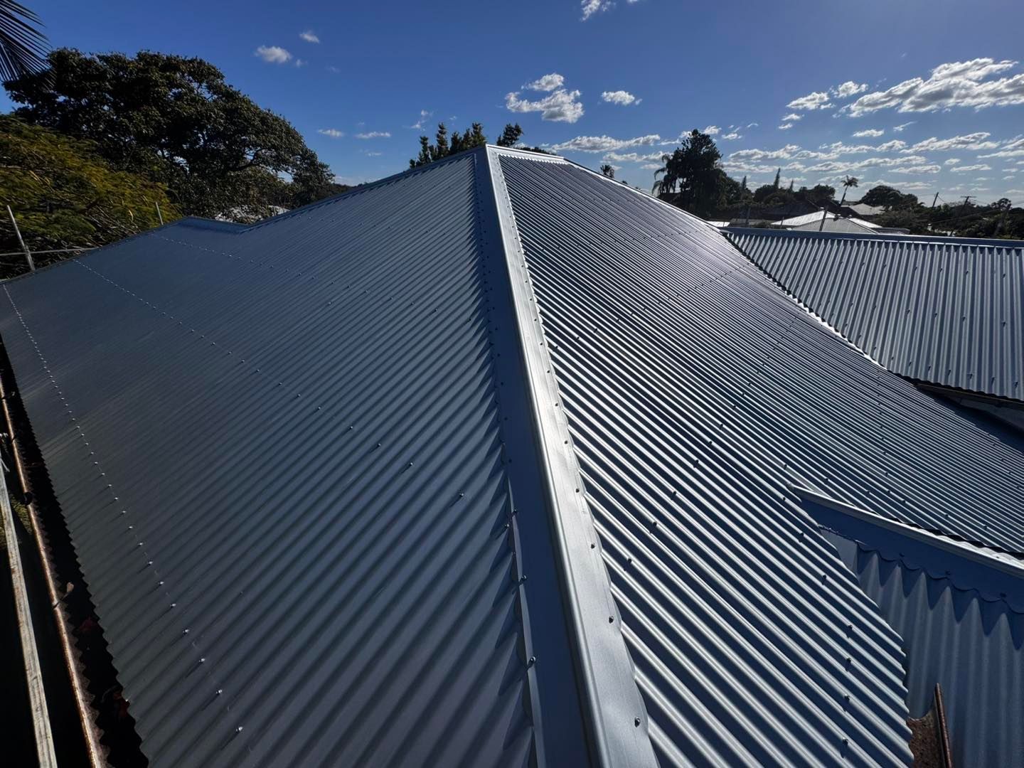 Gray Corrugated Metal Roof Under a Partly Cloudy Blue Sky — Rumara Roofing in Sunshine Coast, QLD