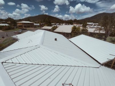 White Metal Roofs of Buildings With Mountain Backdrop Under a Cloudy Sky — Rumara Roofing in Sunshine Coast, QLD