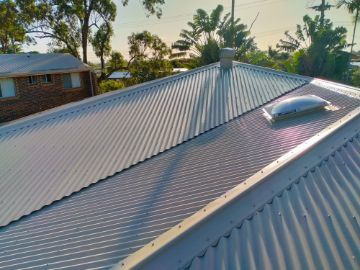 Corrugated Metal Roof With a Skylight, Chimney, and a Home in the Background — Rumara Roofing in Sunshine Coast, QLD