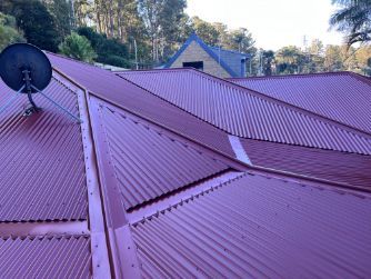Red Metal Roof With Satellite Dish, Set Against Backdrop of Trees and a House — Rumara Roofing in Sunshine Coast, QLD