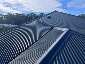 Dark Corrugated Metal Roof With a Blue Sky and Trees in the Background — Rumara Roofing in Sunshine Coast, QLD