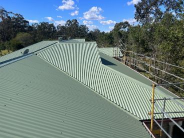 Green Metal Roof Under a Blue Sky With Safety Scaffolding Surrounding Trees — Rumara Roofing in Sunshine Coast, QLD