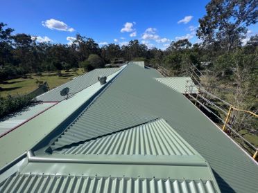 Green Metal Roof With Multiple Sections Against a Background of Trees — Rumara Roofing in Sunshine Coast, QLD