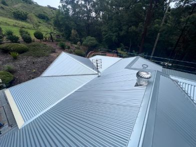 Grey Corrugated Metal Roof on a House, Set Against a Hillside With Trees — Rumara Roofing in Sunshine Coast, QLD